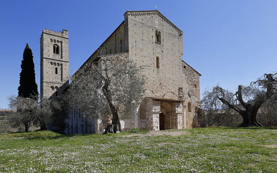 Historic church with stone facade, bell tower, olive trees, and rolling hills.
