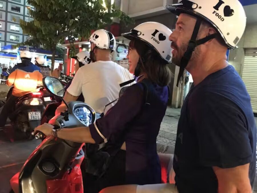 Couple enjoys a scooter ride in Ho Chi Minh City, exploring local cuisine on a night food tour with a local guide.