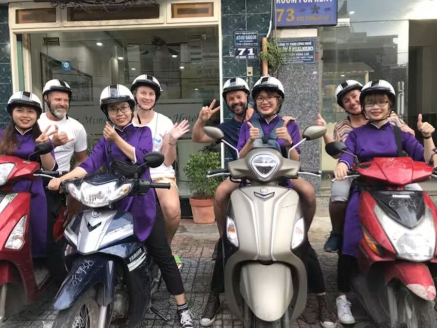People posing on motor scooters, enjoying a night food tour in Ho Chi Minh City led by a local host.