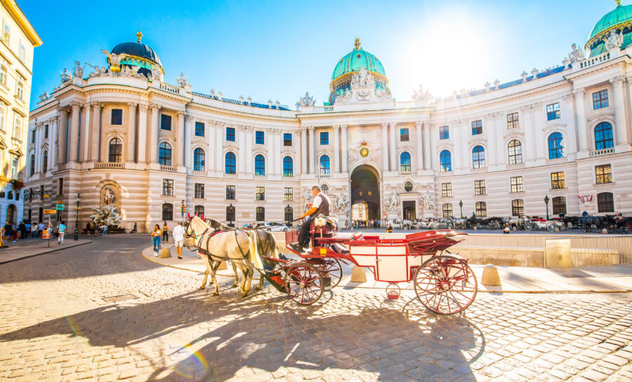 Hofburg Palace with a horse-drawn carriage on a sunny street in Vienna, Austria, showcasing historic architecture and vibrant atmosphere