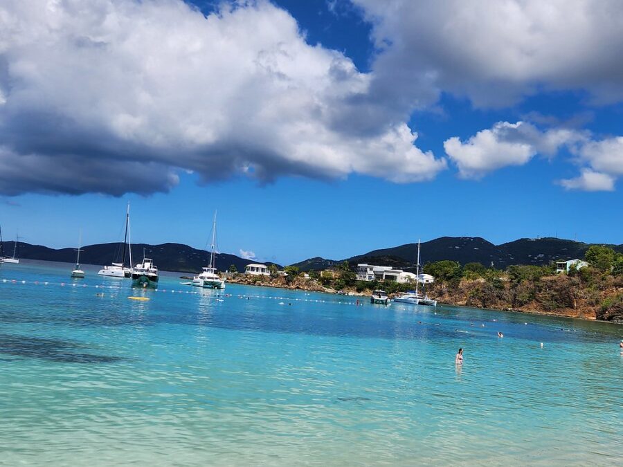 Boats float in the clear blue waters of Honeymoon Beach, St. Thomas, with a picturesque sandy beach in the foreground.