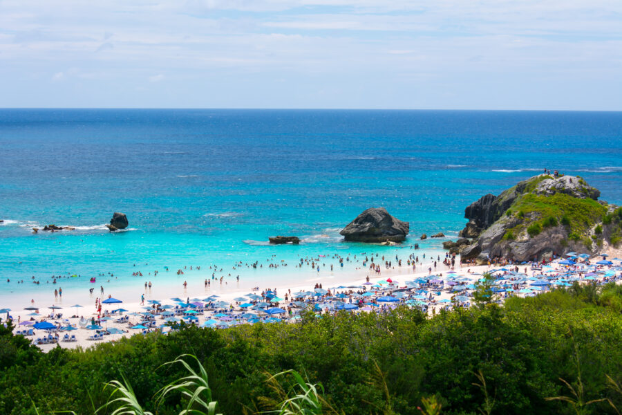 Tourists relax on the sandy shores of Horseshoe Bay, Bermuda, with a stunning panoramic view of the coastline.