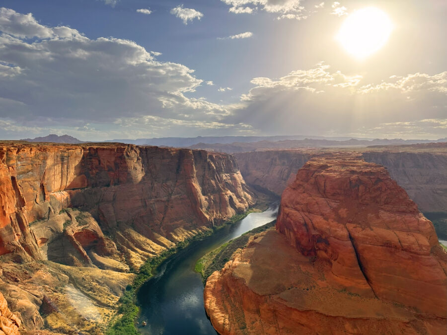 Scenic panorama of Horseshoe Bend in the Grand Canyon under bright sunlight, highlighting the river's dramatic bend and rock formations