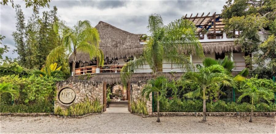 Entrance to Hotel Aires Bacalar in Mexico, featuring palm trees and a thatched roof, welcoming guests to the resort