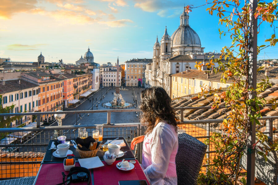 From a rooftop terrace, a woman savors her breakfast while taking in the stunning view of Rome and Piazza Navona.