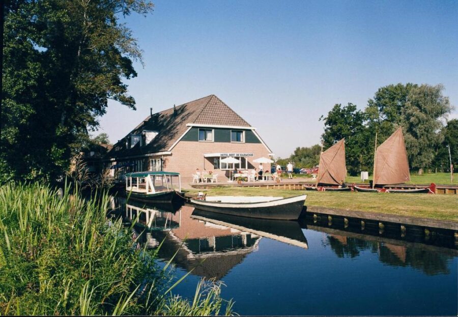 Hotel de Harmonie with a house adjacent to a boat floating on calm waters, creating a picturesque waterfront scene.
