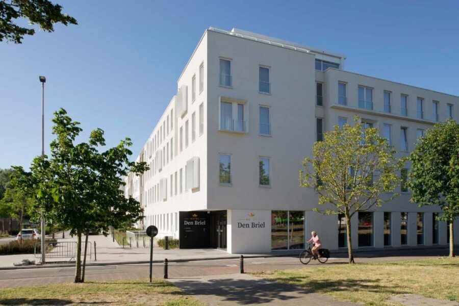 Hotel Den Briel, a white building, stands in Ghent with a tree positioned in front of it.
