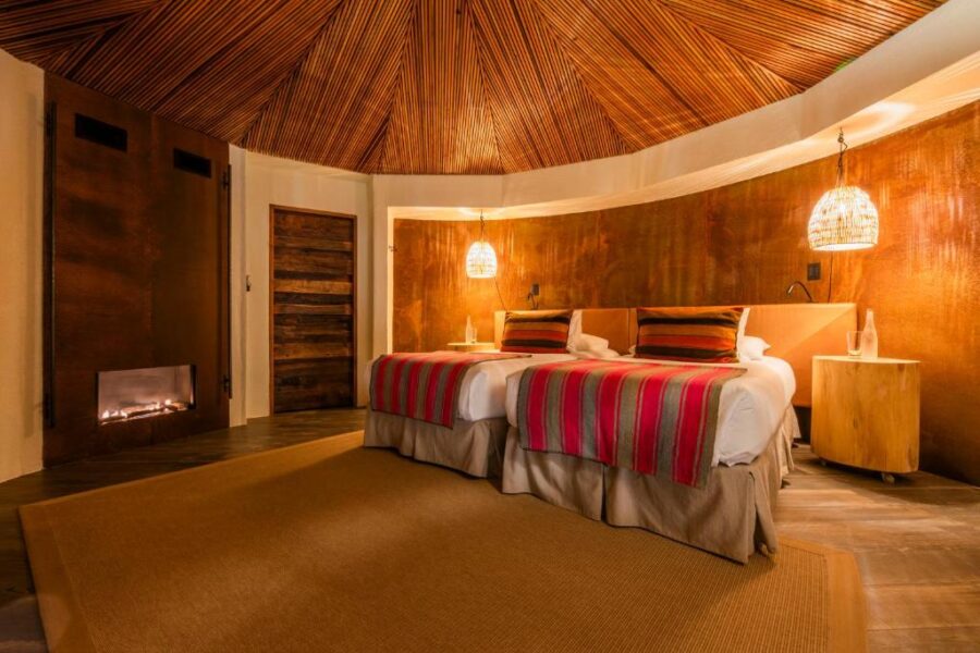 Inside Hotel Desertica, a charming bedroom with a wooden ceiling and two beds, located in San Pedro de Atacama, Chile.
