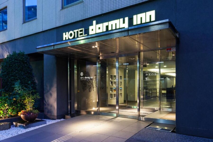 Dormy Inn Kanazawa hotel entrance at night with illuminated sign, modern lobby, and landscaped walkway.