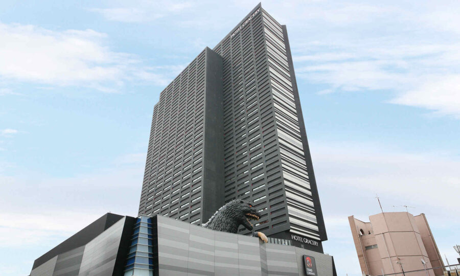 Godzilla statue on Hotel Gracery Shinjuku podium beneath Tokyo skyscraper.