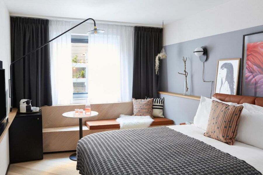 Interior of a Hotel Indigo room in Antwerp, showcasing a bed, a chair, and a window for natural illumination.
