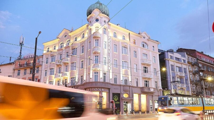 Bus passes by the Hotel Lion Sofia, featuring a prominent clock on its facade.