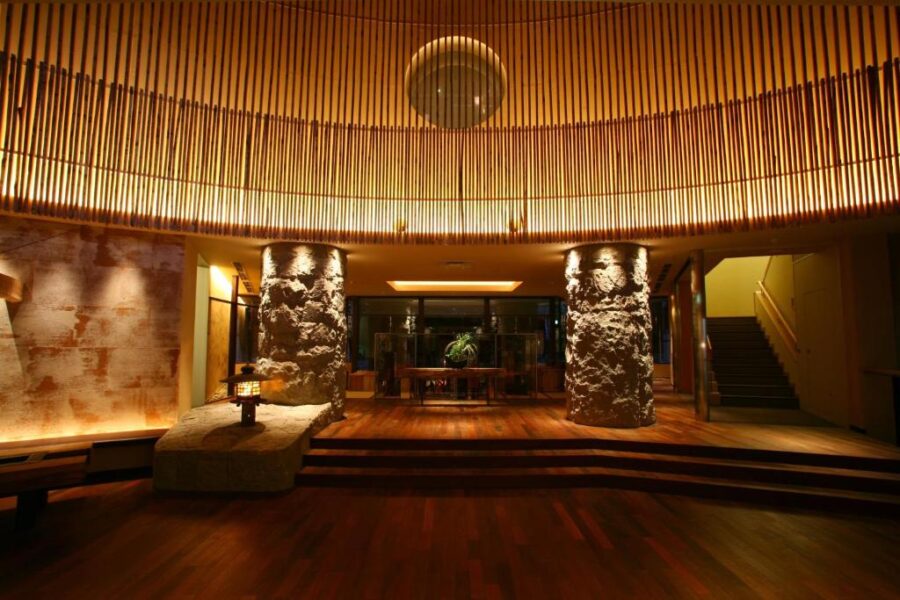 Luxury hotel lobby with warm wood, stone columns, ambient lighting, and modern Japanese interior design.