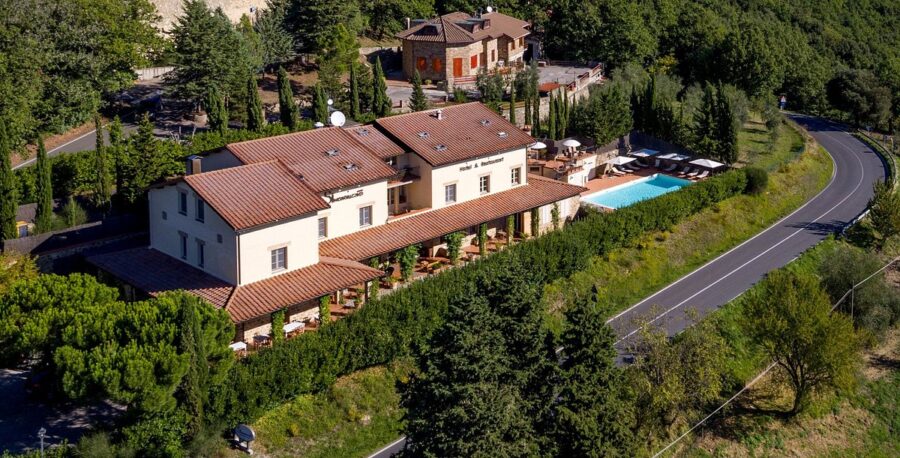 Charming countryside hotel with terracotta roofs, lush greenery, pool, and outdoor seating.