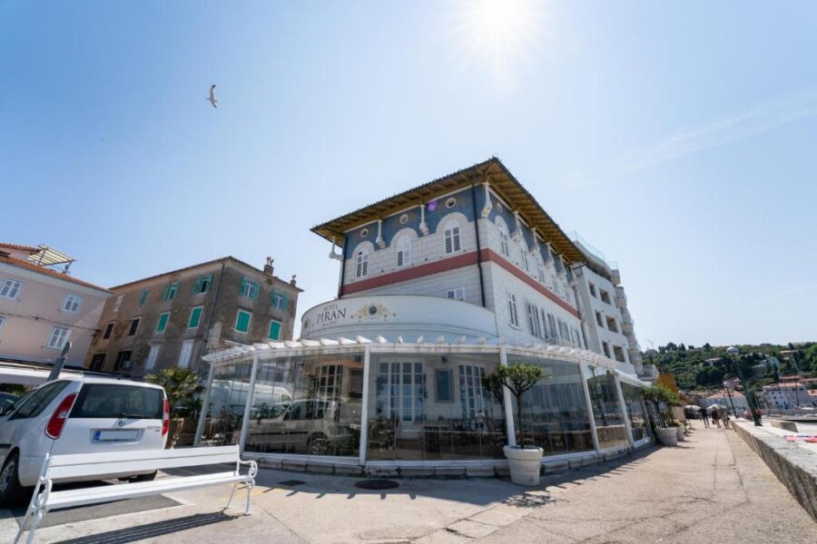 Historic coastal building of Hotel Piran in Piran, Slovenia under a bright sun, with an elegant facade and glass-enclosed patio