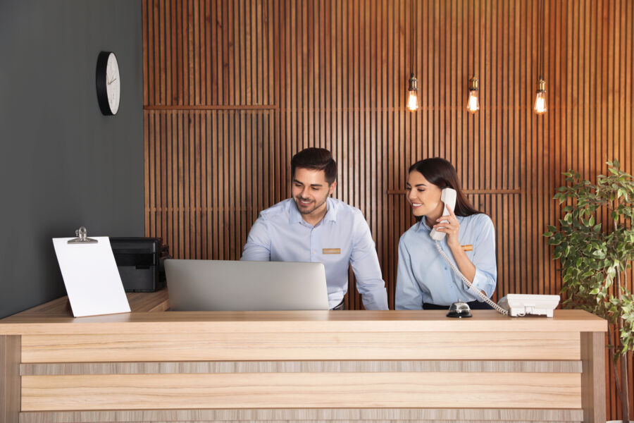 Receptionists assist guests at a sleek desk in a contemporary hotel lobby with modern decor and welcoming atmosphere.