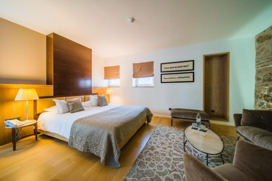 Cozy hotel room at Hotel Vestibul Palace, featuring a bed, chair, and lamp in a warm, inviting setting.