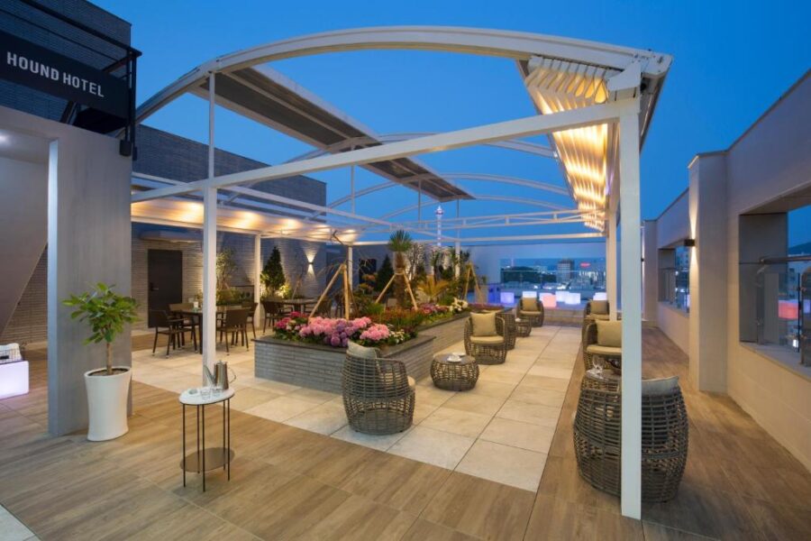 Modern Hound Hotel rooftop terrace lounge at dusk with pergola, seating, garden, and city views.