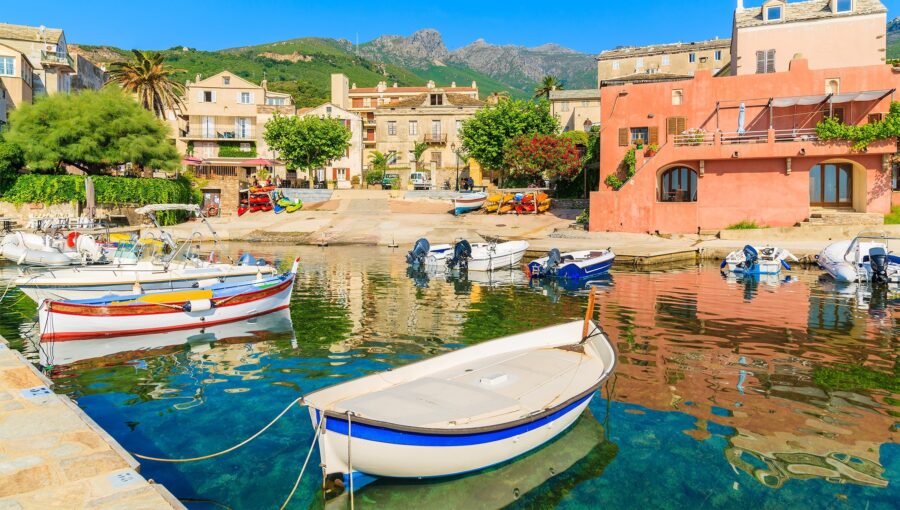 Charming coastal village harbor with colorful boats, vibrant facades, and mountain backdrop.