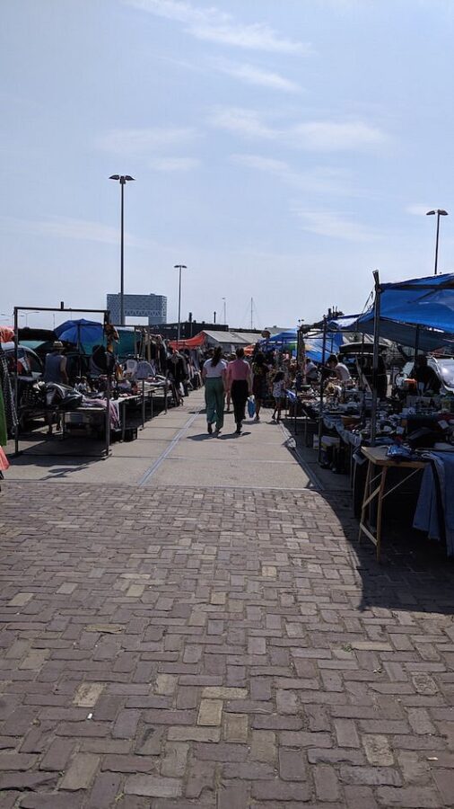Bustling IJ-Hallen Amsterdam flea market filled with people browsing various tents and stalls.