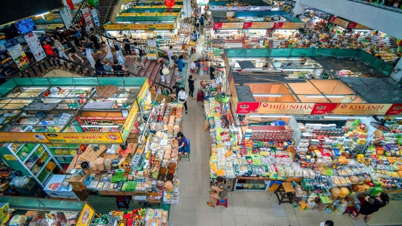 Busy Vietnamese indoor food market with colorful stalls, local vendors, and shoppers browsing traditional products.