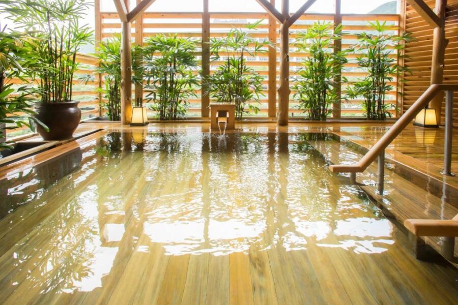 Indoor Japanese onsen with wooden soaking pool, bamboo plants, tranquil spa retreat atmosphere.