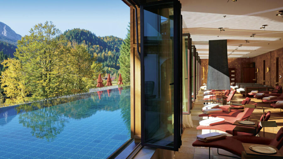 Modern spa with infinity pool, glass windows, red lounge chairs, and stunning mountain views.
