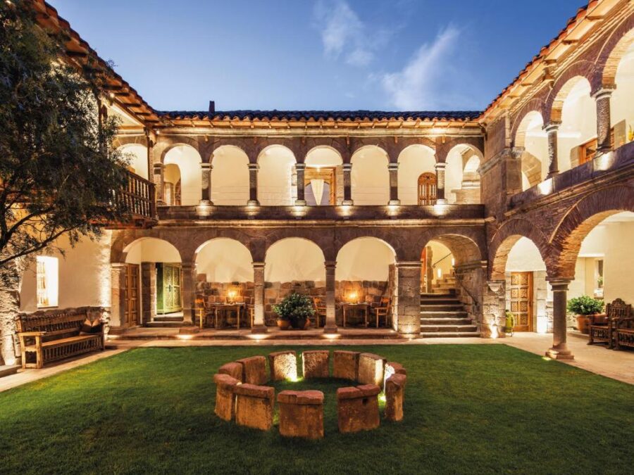 Nighttime view of the courtyard at Inkaterra La Casona hotel in Cusco, Peru, featuring soft lighting and lush greenery.