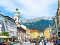 Busy Innsbruck town center filled with people enjoying street cafes against a backdrop of Tyrolean architecture.
