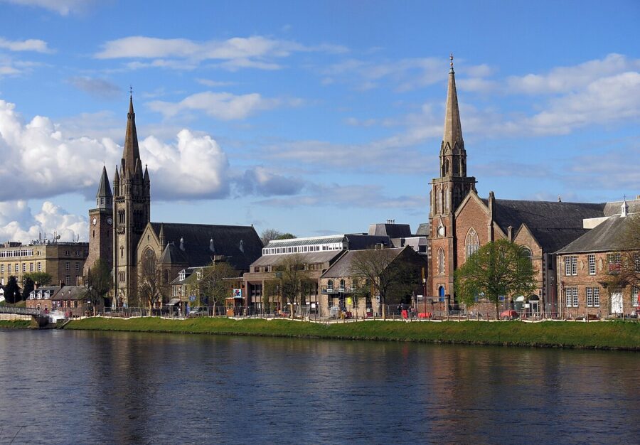 Tranquil waters in Inverness, Bank Street, Scotland, surrounded by lush greenery and distant hills.