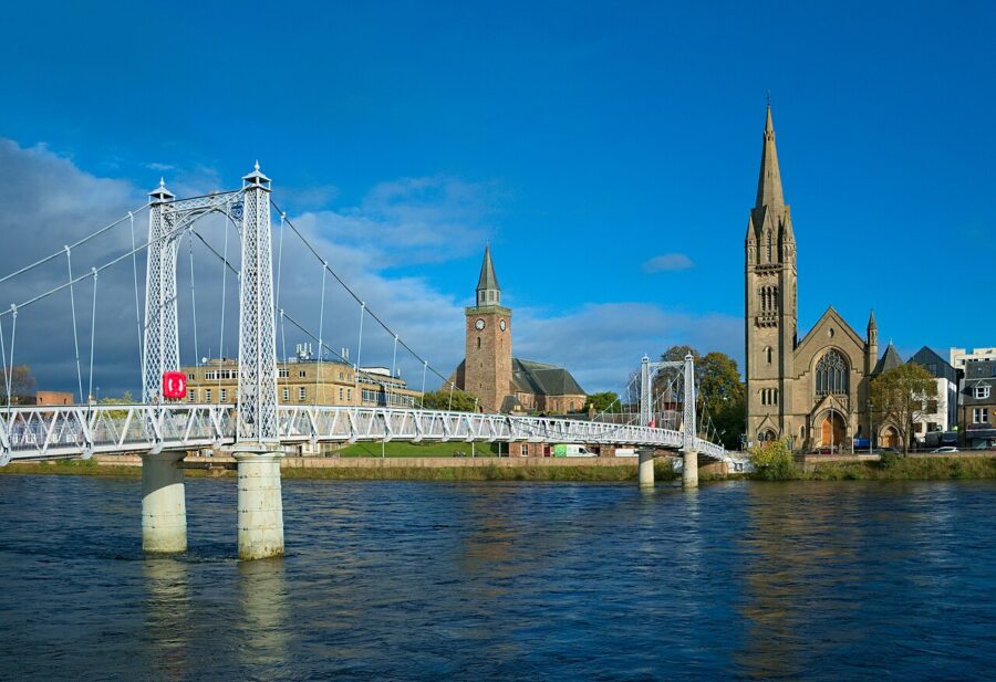 Inverness's Greig Street Bridge crosses a river, featuring a church in the backdrop against a scenic landscape.