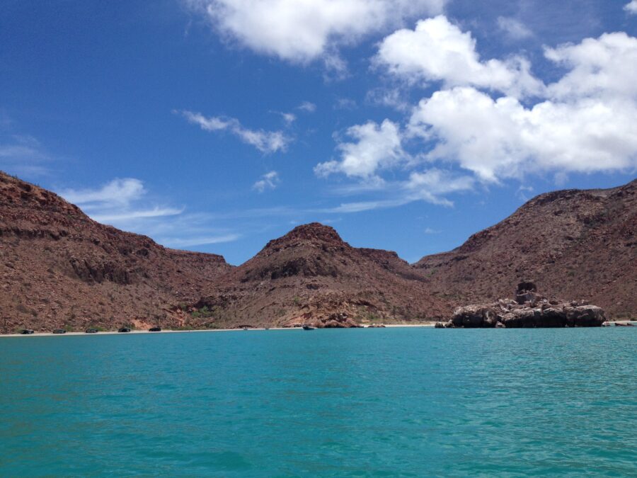 Tranquil waters of Isla Espíritu Santo in Mexico, reflecting the sky and bordered by rugged cliffs and lush vegetation.