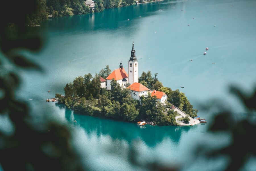 Idyllic island with church, lake, verdant trees, and serene boats under clear sky.