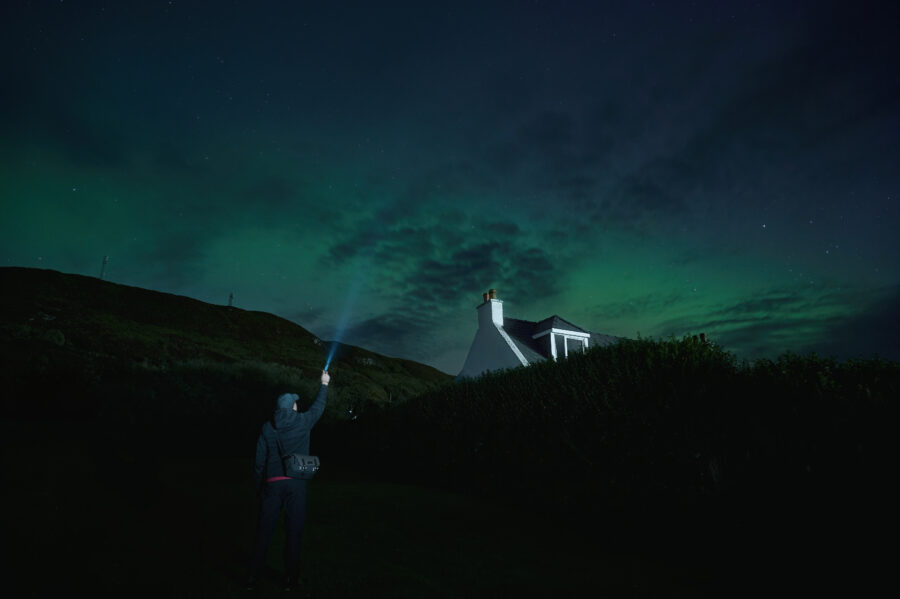 Northern lights illuminate the sky as a man stands outside a house on the Isle of Skye, Scotland.
