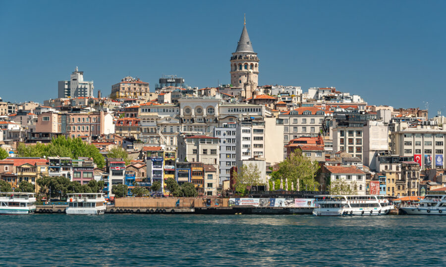 Waterfront view of Istanbul with Galata Tower, boats, and diverse architecture under clear skies.