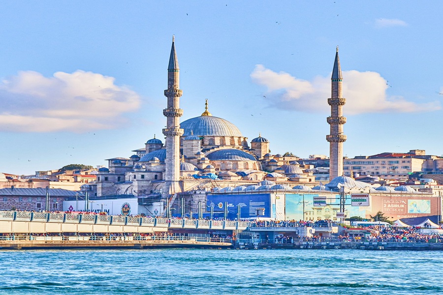 Historic Istanbul mosque with domes, minarets, waterfront, and vibrant city life under blue sky.
