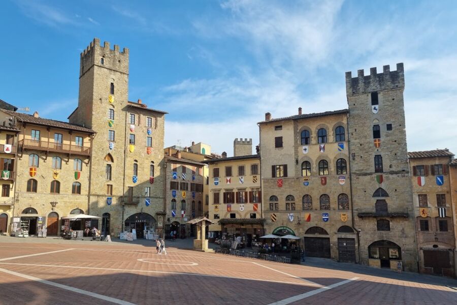 Medieval Arezzo square with stone towers and rustic facades, lively social hub with people.