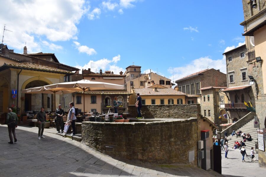 Charming Cortona street with historic architecture, cobblestone, outdoor dining, and vibrant community life.