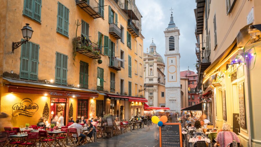 Charming European coastal street with diners and historic architecture at dusk.