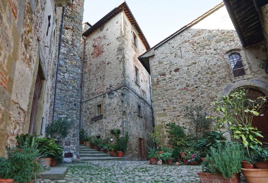 Charming stone courtyard with lush greenery, historic buildings, and inviting ambiance in Italian village.