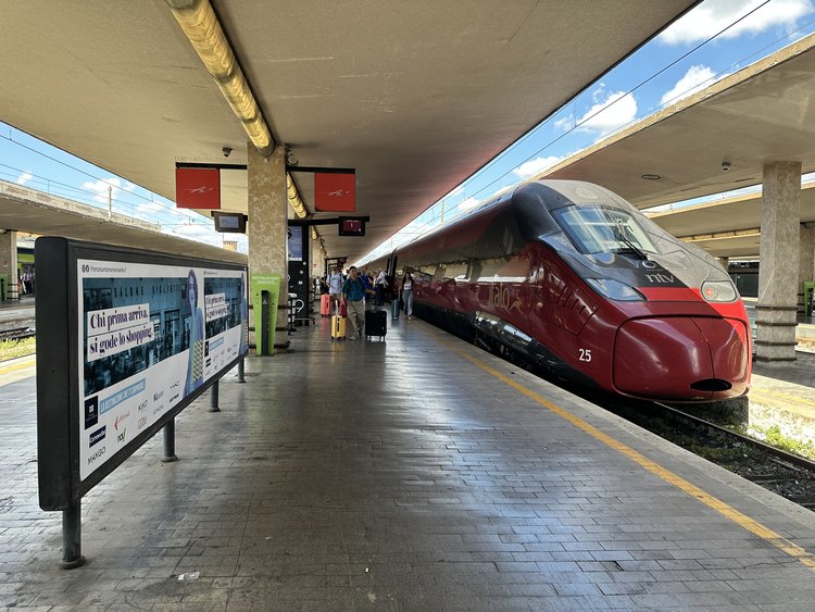 Red Italo high-speed train at Florence railway station platform under modern concrete canopy.