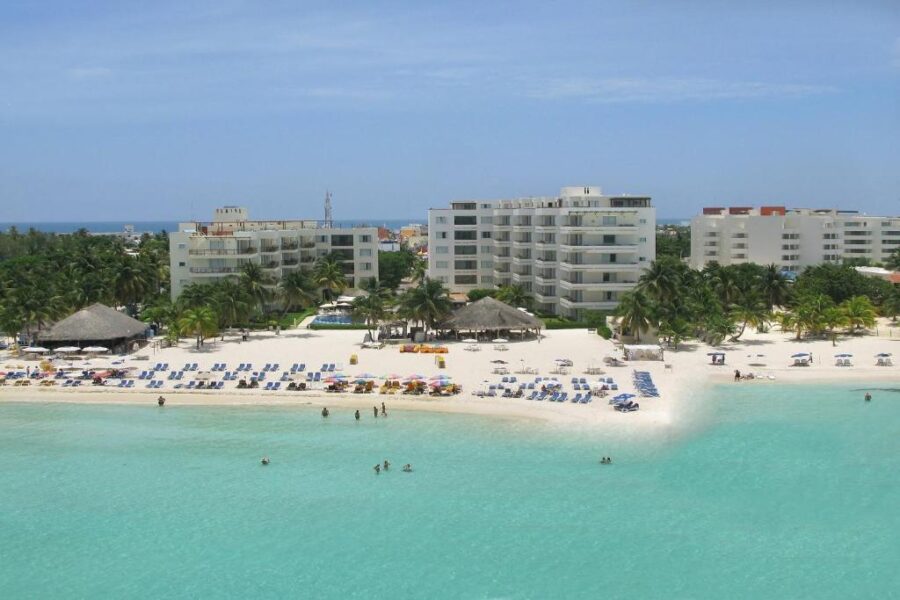 Ixchel Beach Hotel in Isla Mujeres, Mexico, featuring a sandy beach with a few visitors relaxing under the sun.
