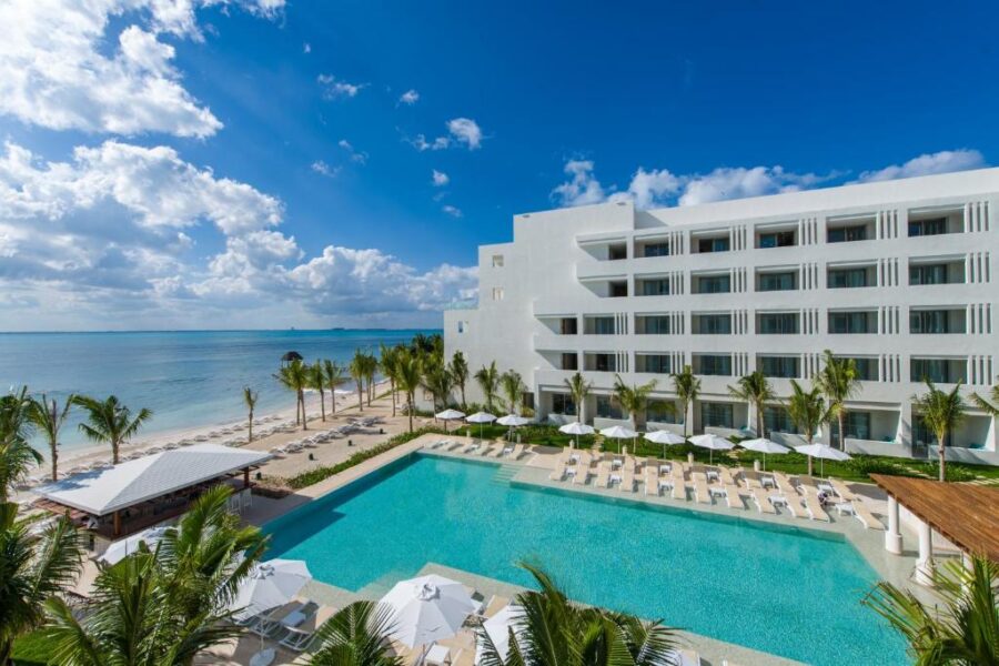 The white Izla Beach Front Hotel situated on the beach in Isla Mujeres, Mexico, with a view of the ocean.