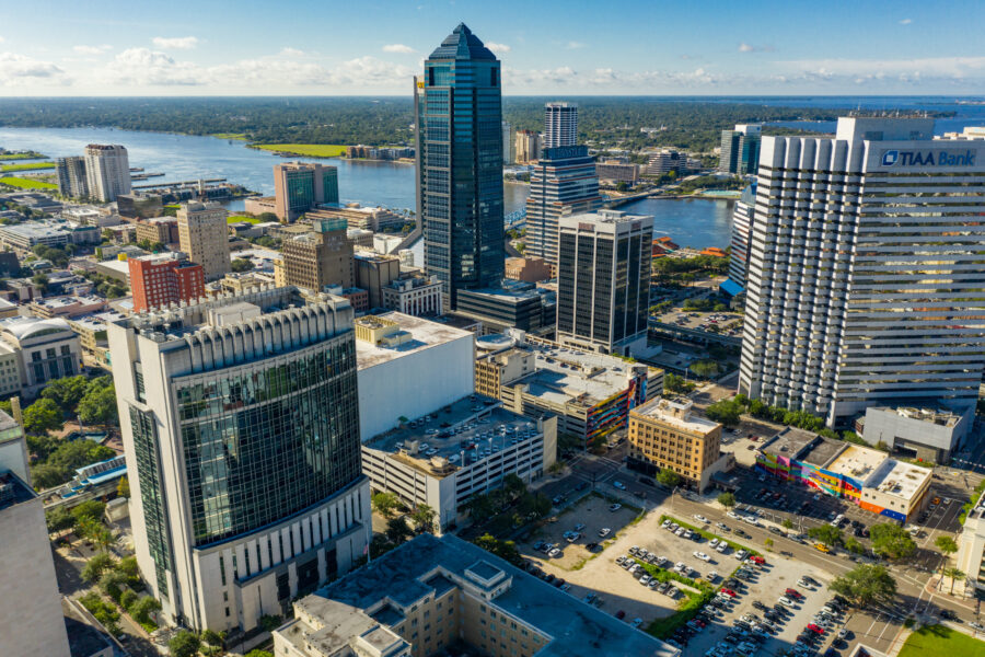 Aerial view of Jacksonville, FL, showcasing the cityscape and various buildings against a clear blue sky.