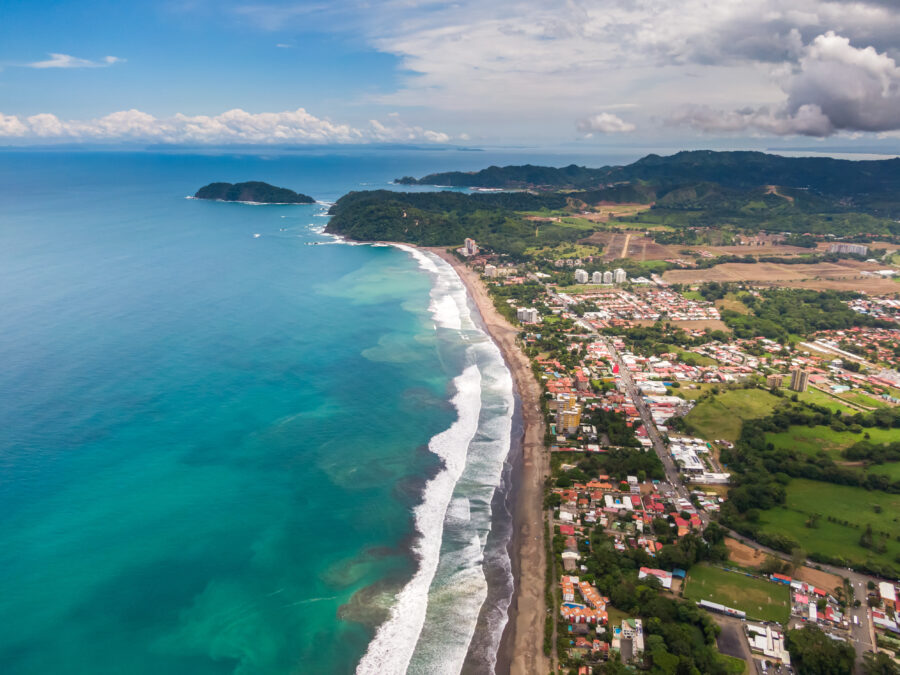 Aerial view of Jaco Beach in Costa Rica, showcasing golden sands, turquoise waters, and lush green hills in the background