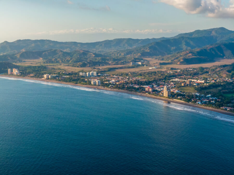 Aerial view of Jaco Beach town in Costa Rica, showcasing sandy beaches, vibrant buildings, and lush green hills