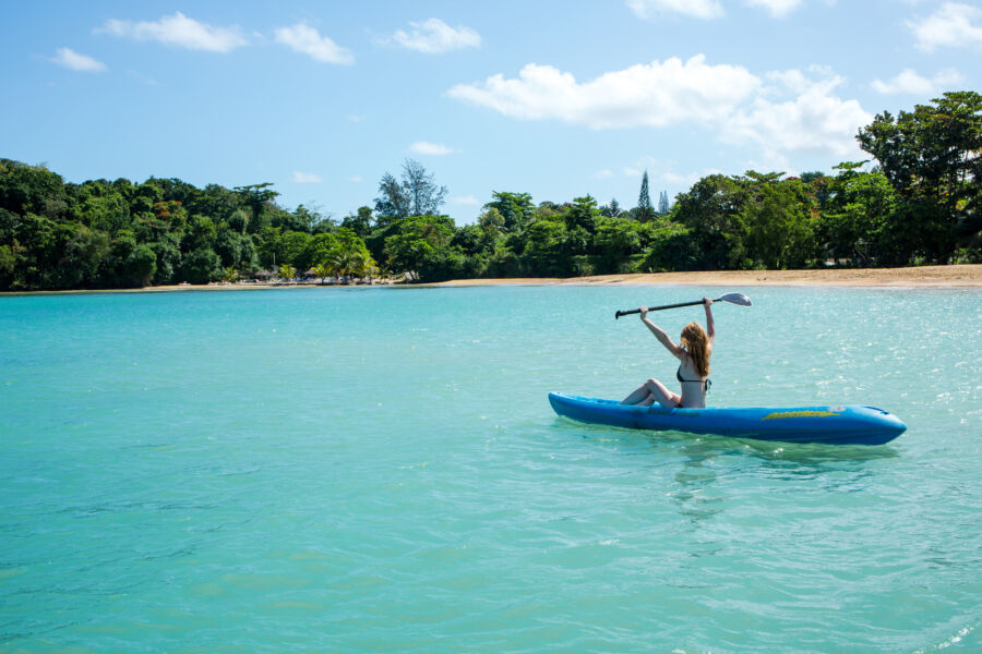 Woman enjoys kayaking in the vibrant Caribbean waters of Jamaica, with lush greenery in the background