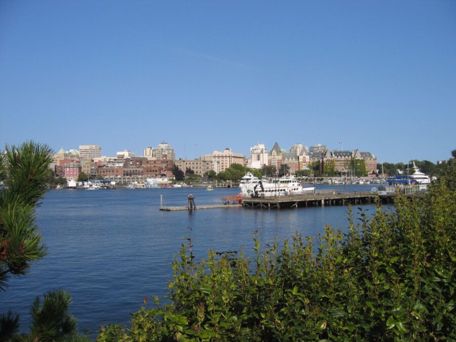 Panoramic view of the city of Victoria from a dock at James Bay, showcasing buildings and boats against the water.