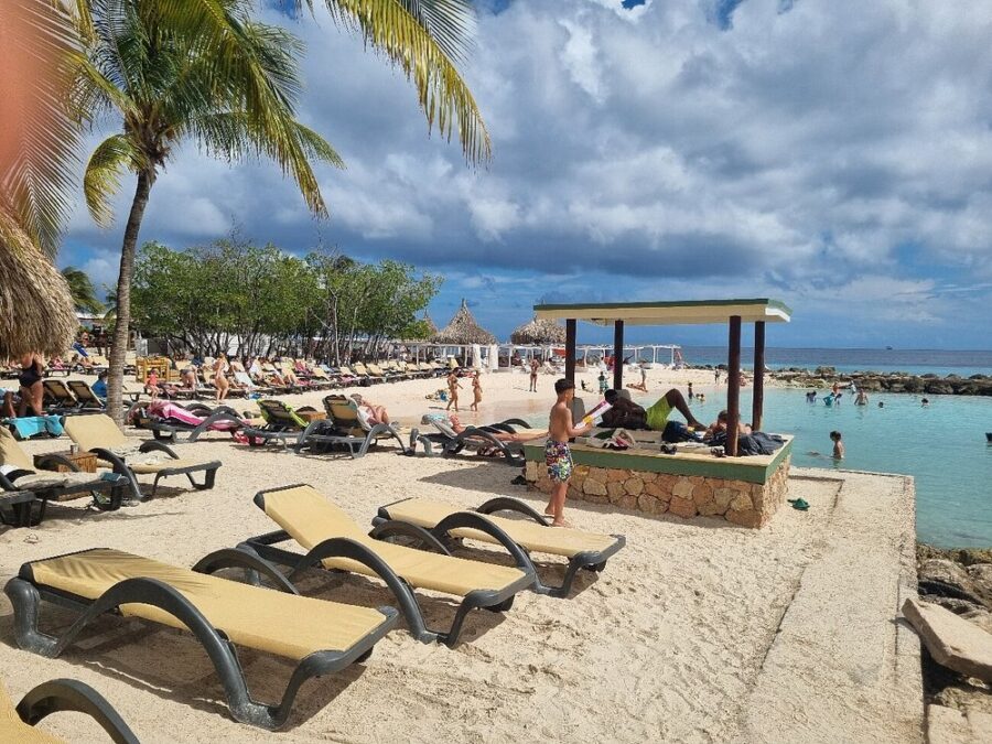 Lounge chairs and colorful umbrellas line Jan Thiel Beach in Willemstad, Curacao, with gentle waves in the background.
