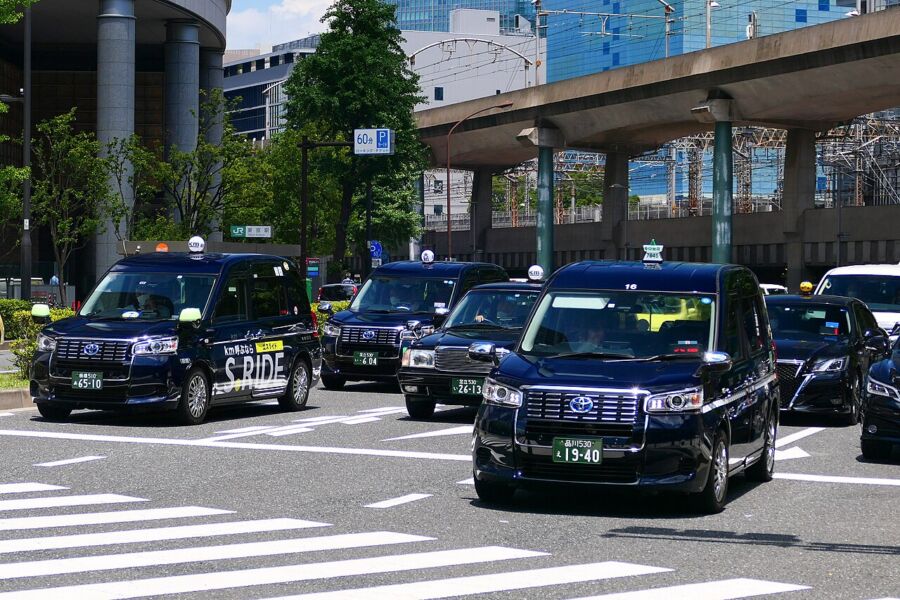 Several Japanese taxis lined up on the road, highlighting their unique styles and bright colors.

